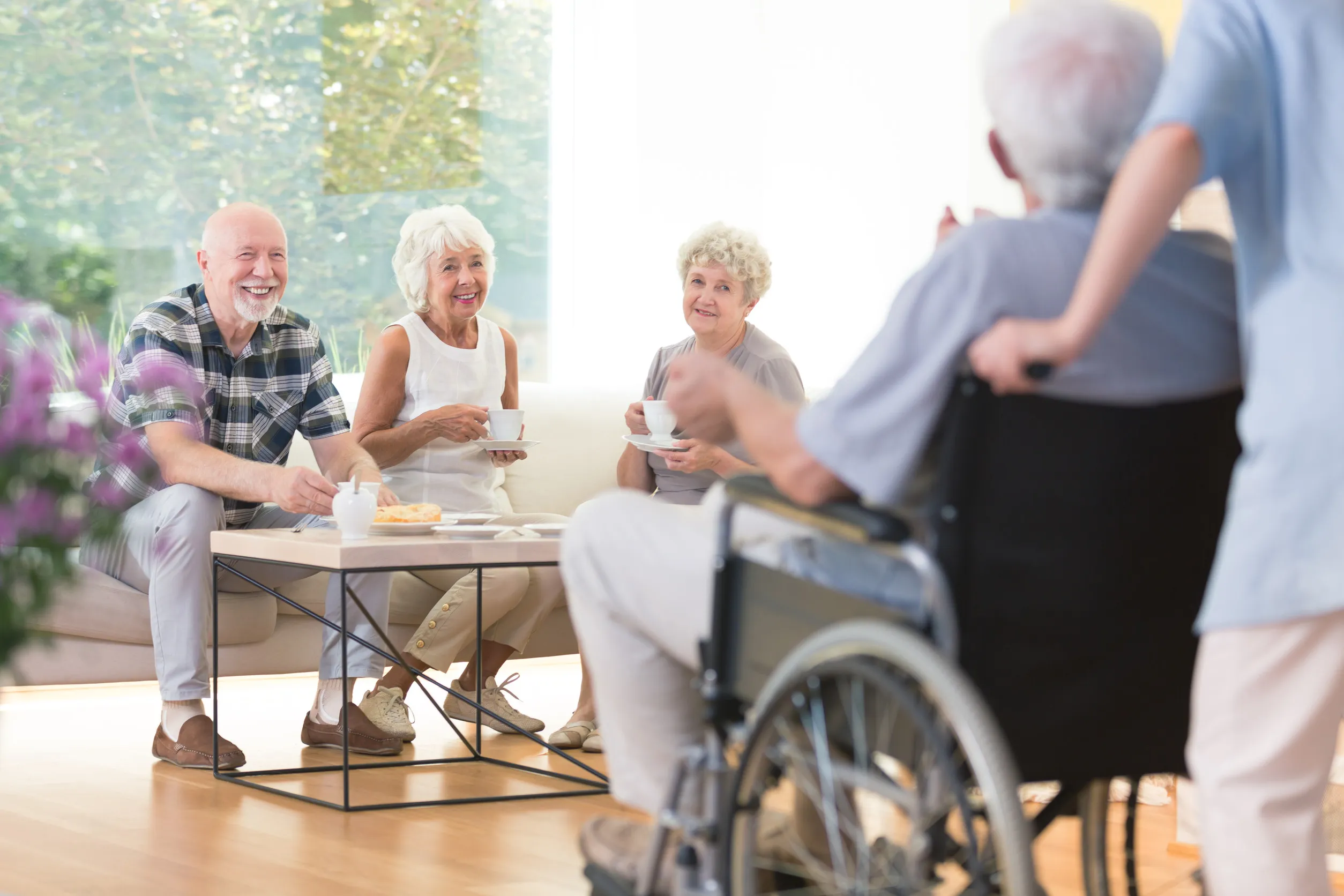 Happy seniors sitting on the couch and visiting their disabled friend at a nursing house Happy seniors sitting on the couch and visiting their disabled friend at a nursing house